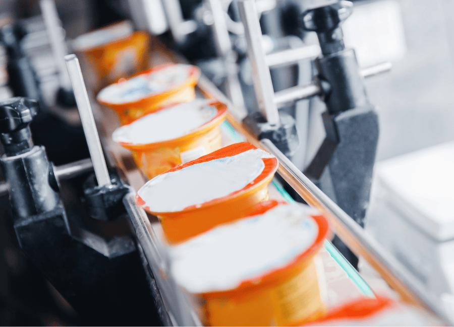 Orange yogurt cups on a conveyor that applies label and lid