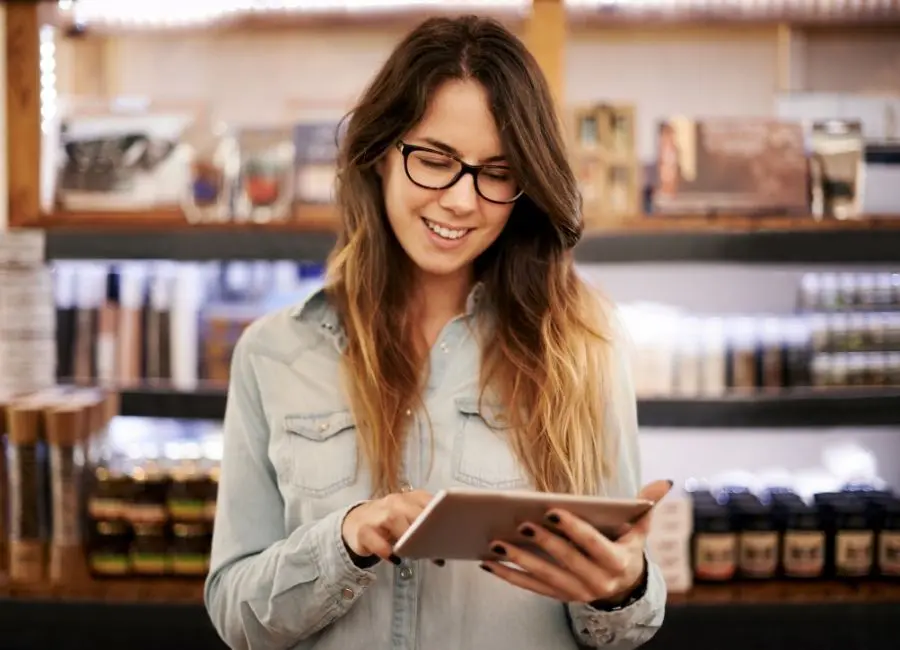 A young woman with glasses holds a tablet with food industry artificial intelligence tools in her soft-lit coffee shop
