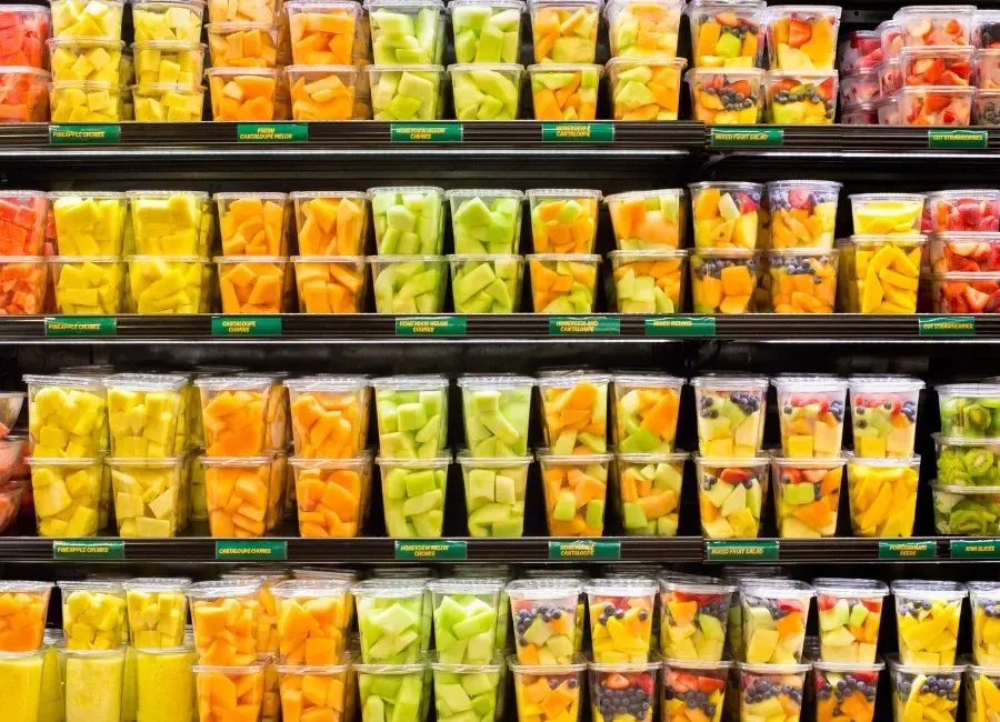Refrigerated grocery display filled with clear cups of fresh cut pineapple, melon, mango, berries, and mixed fruit.