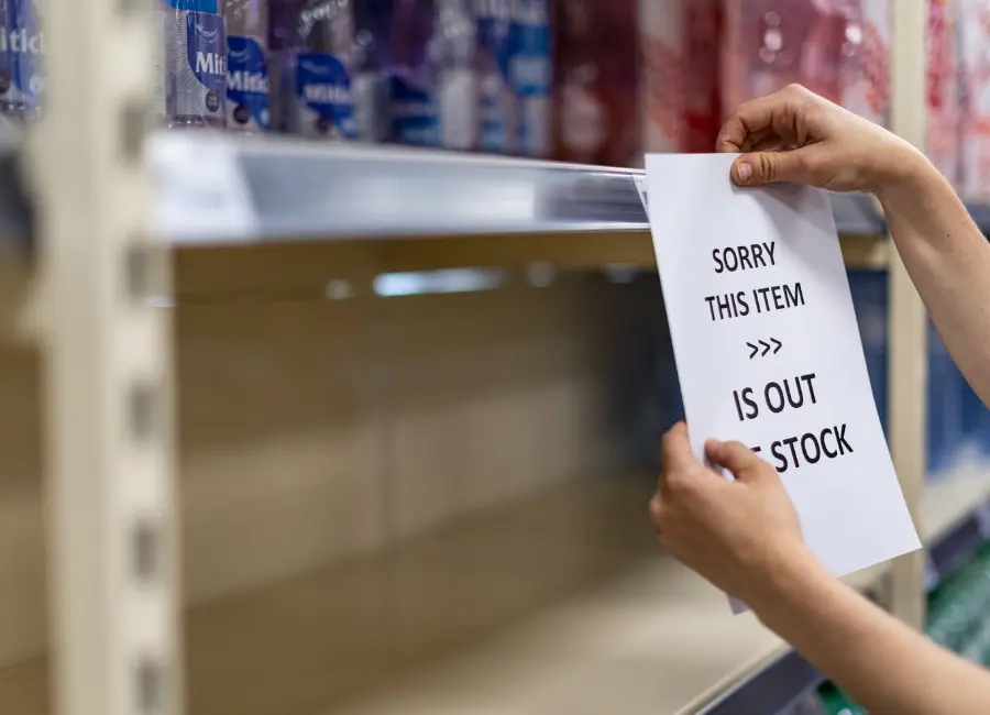 Person placing an out-of-stock sign on an empty retail store shelf, highlighting product shortages and inventory availability.