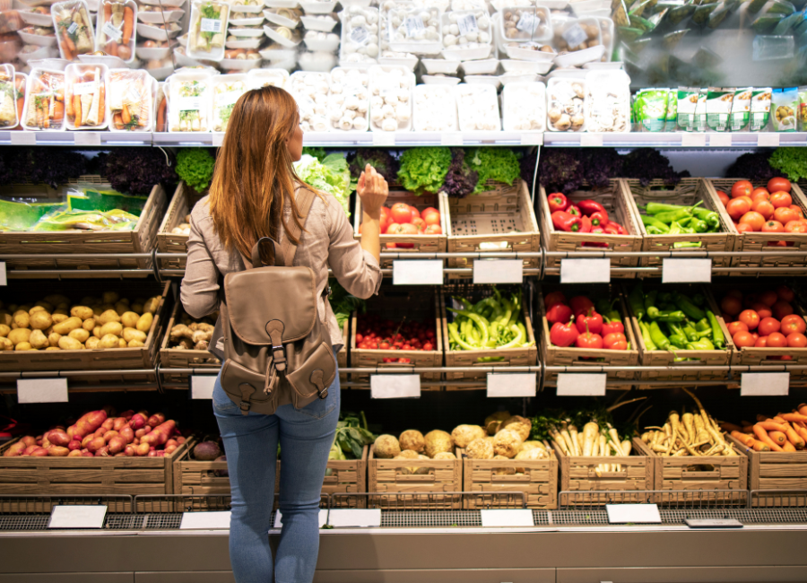 Woman with backpack selecting fresh vegetables from well-stocked supermarket produce section