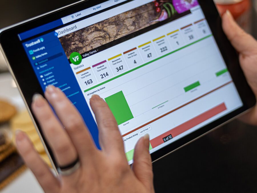 A portable tablet showing the FoodLogiQ Compliance dashboard.