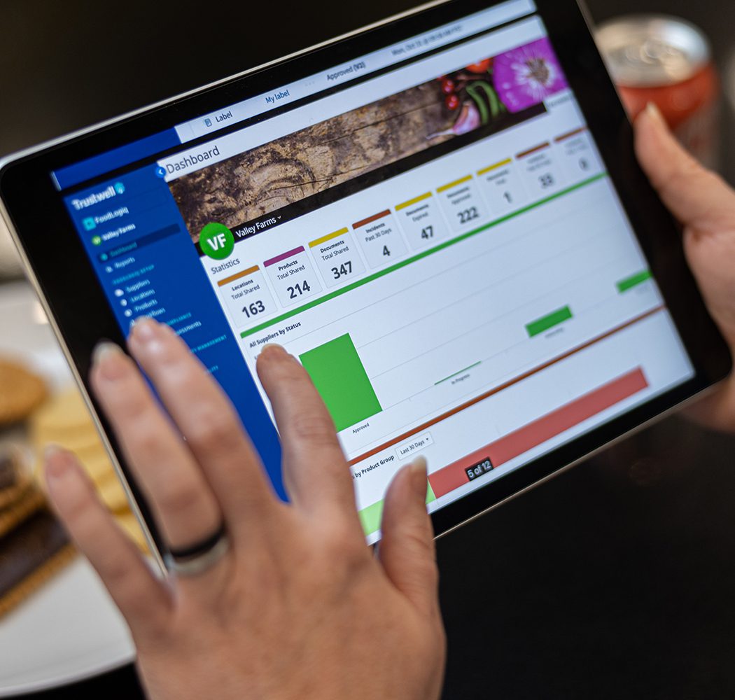 A portable tablet showing the FoodLogiQ Compliance dashboard.