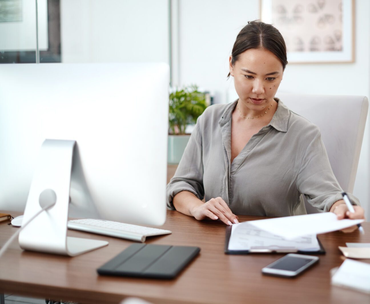 Professional woman reviews documents at a desk with computer and devices.