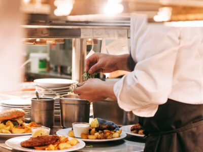 Food orders on the kitchen table in the restaurant, chief decorating schnitzel and fried potatoes, traditional german plate