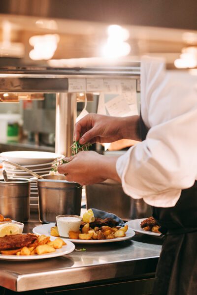 Food orders on the kitchen table in the restaurant, chief decorating schnitzel and fried potatoes, traditional german plate