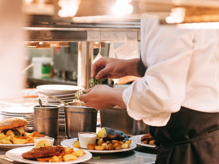 Food orders on the kitchen table in the restaurant, chief decorating schnitzel and fried potatoes, traditional german plate