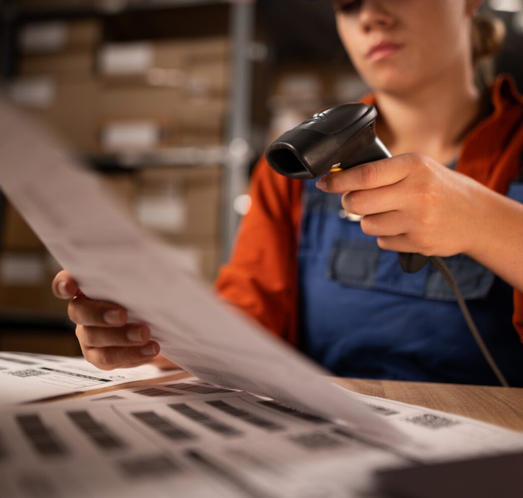 Close up of warehouse worker scanning barcodes on paper working in a large warehouse, sitting at table