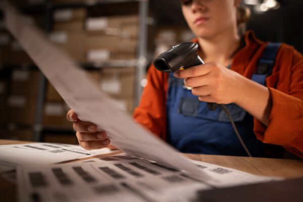 Close up of warehouse worker scanning barcodes on paper working in a large warehouse, sitting at table