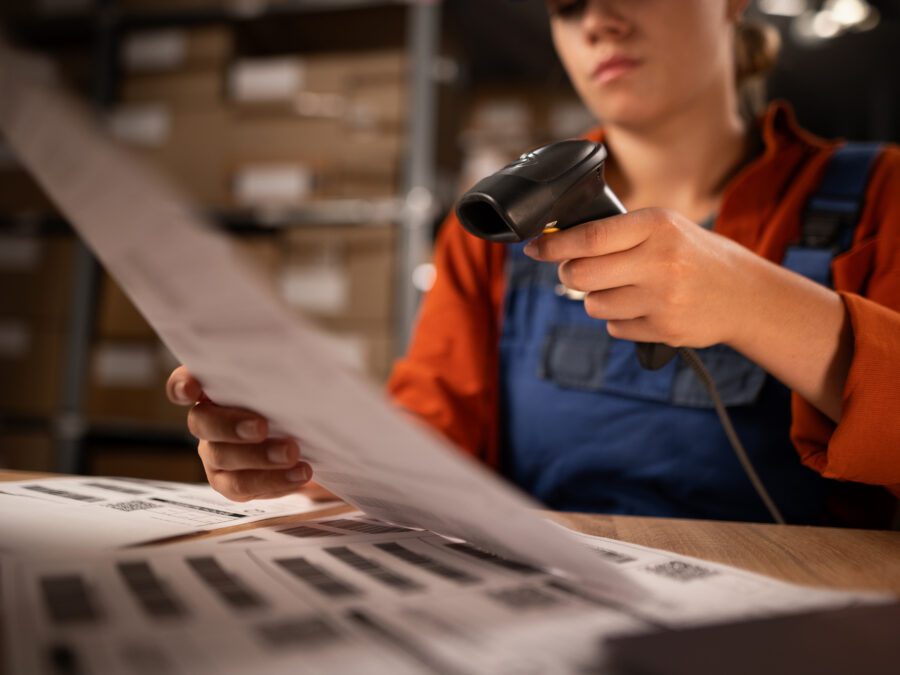 Close up of warehouse worker scanning barcodes on paper working in a large warehouse, sitting at table