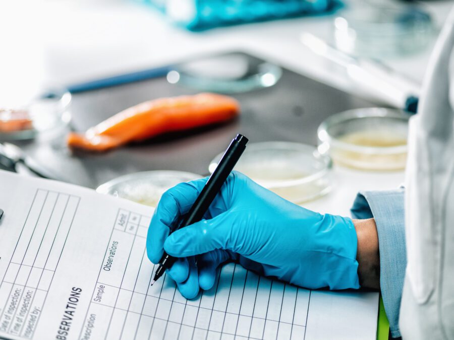 Food safety and quality management. Food safety and quality inspector filling out quality control form in a laboratory, salmon in background