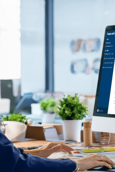 Woman in blazer typing at desktop computer showing Taskwell help document.
