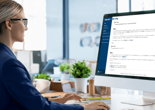 Woman in blazer typing at desktop computer showing Trustwell's AskReg