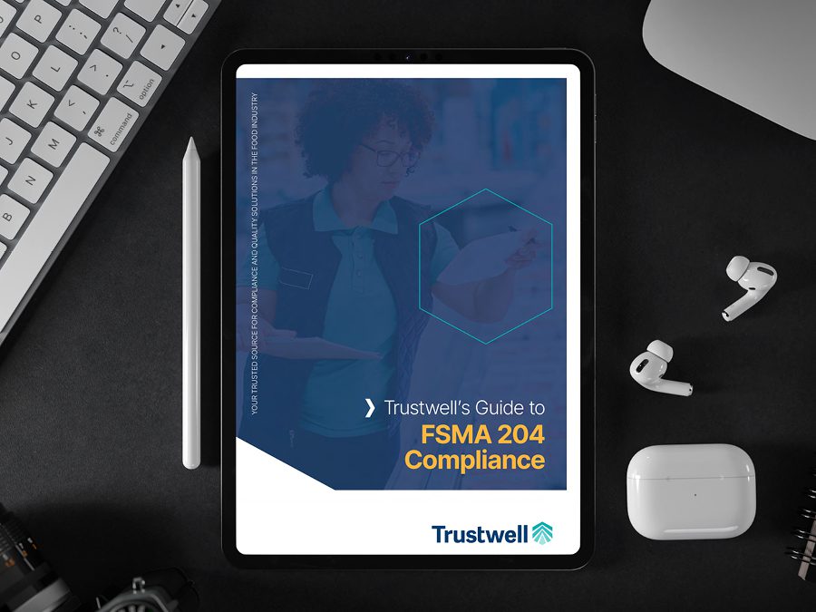 Tablet displaying Trustwell's FSMA 204 Compliance Guide surrounded by office items.
