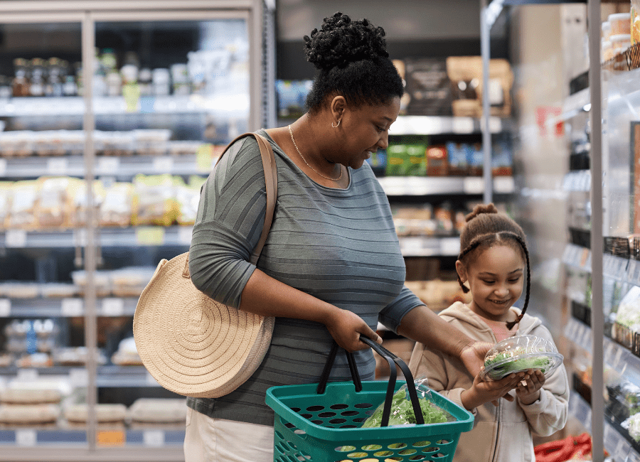 Mother and daughter grocery shopping in supermarket produce section, viewing a container of lettuce