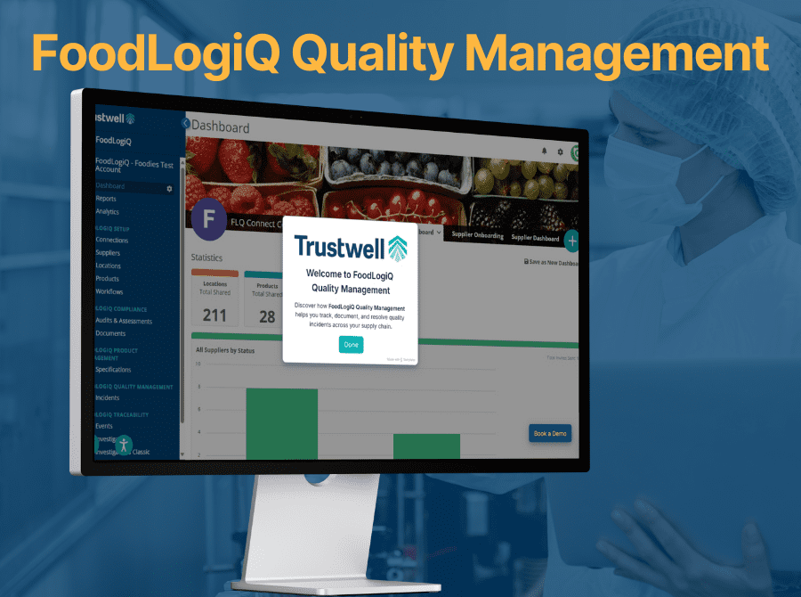 Monitor displaying Trustwell’s FoodLogiQ Quality Management dashboard, with food safety worker in protective gear in the background.