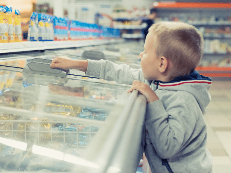 Young boy reaching into grocery freezer aisle, highlighting need for clear food labeling to prevent recalls.
