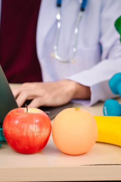 A nutritionist at a desk with fresh fruits, vegetables, dumbbells, and a measuring tape, promoting healthy living.