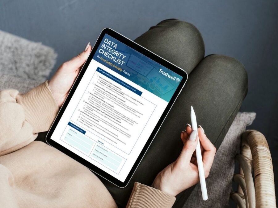 Woman holding a tablet with a Trustwell data integrity checklist for food safety and quality teams, seated with a stylus in hand.