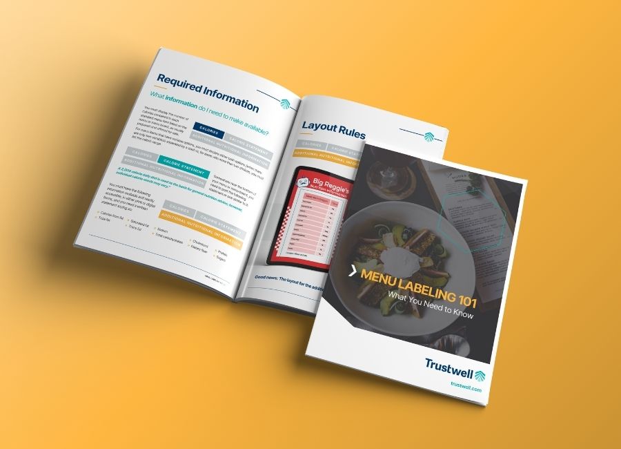 Open eBook on a yellow surface showing menu labeling guidelines and a front cover titled “Menu Labeling 101” by Trustwell.