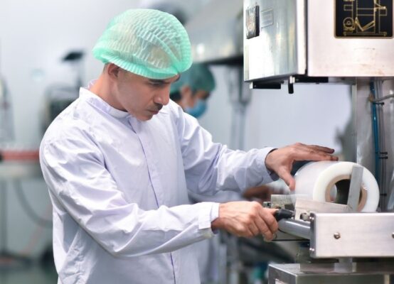 Food production worker in cleanroom attire adjusting a labeling machine to fix food labeling errors in a food production facility