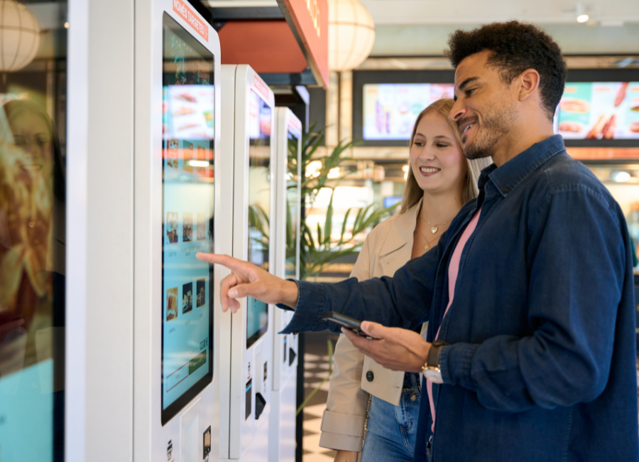 Couple uses a touchscreen self-service kiosk to browse and order food inside a casual restaurant.