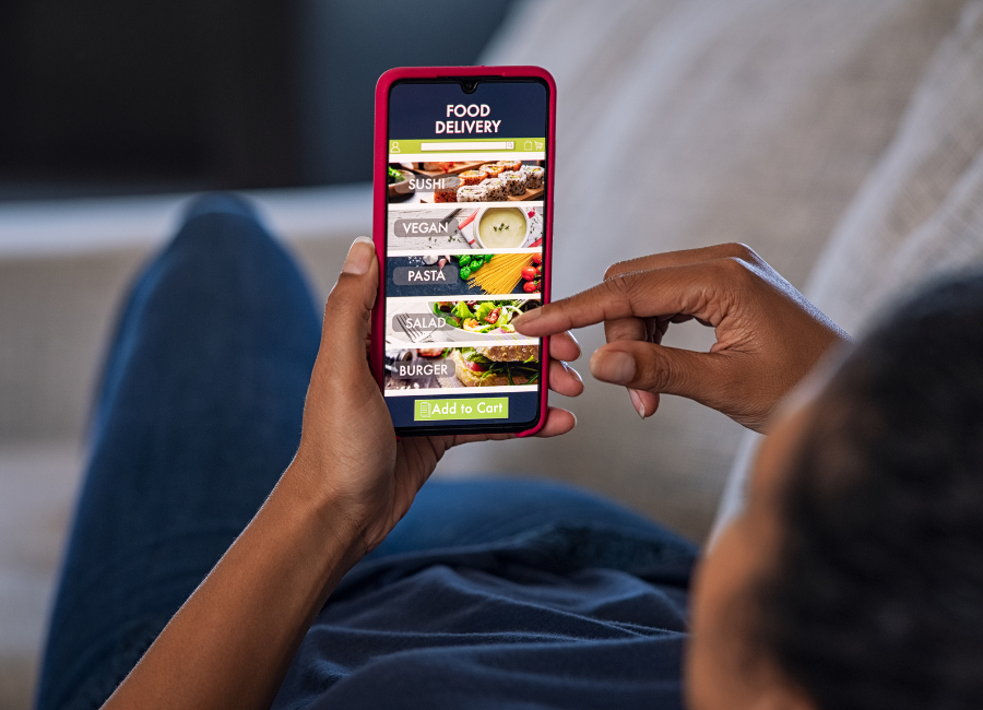 Customer taps a smartphone food delivery app showing sushi, vegan, pasta, salad, and burger menu options.